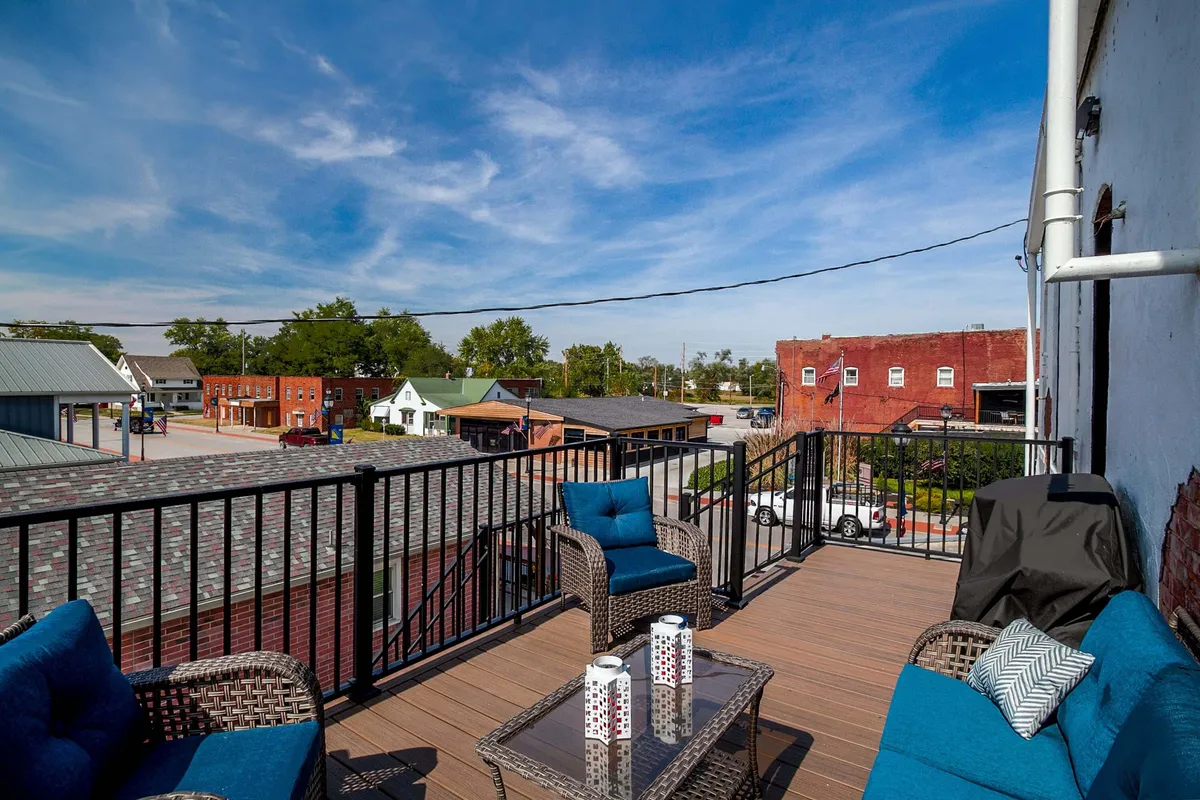 This exterior image showcases an inviting outdoor seating area equipped with comfortable chairs, decorative pillows, and a coffee table. The terrace overlooks the town, creating a scenic backdrop perfect for evening relaxation or social gatherings. The historic character of the surrounding building is subtly visible, emphasizing the space's unique charm.