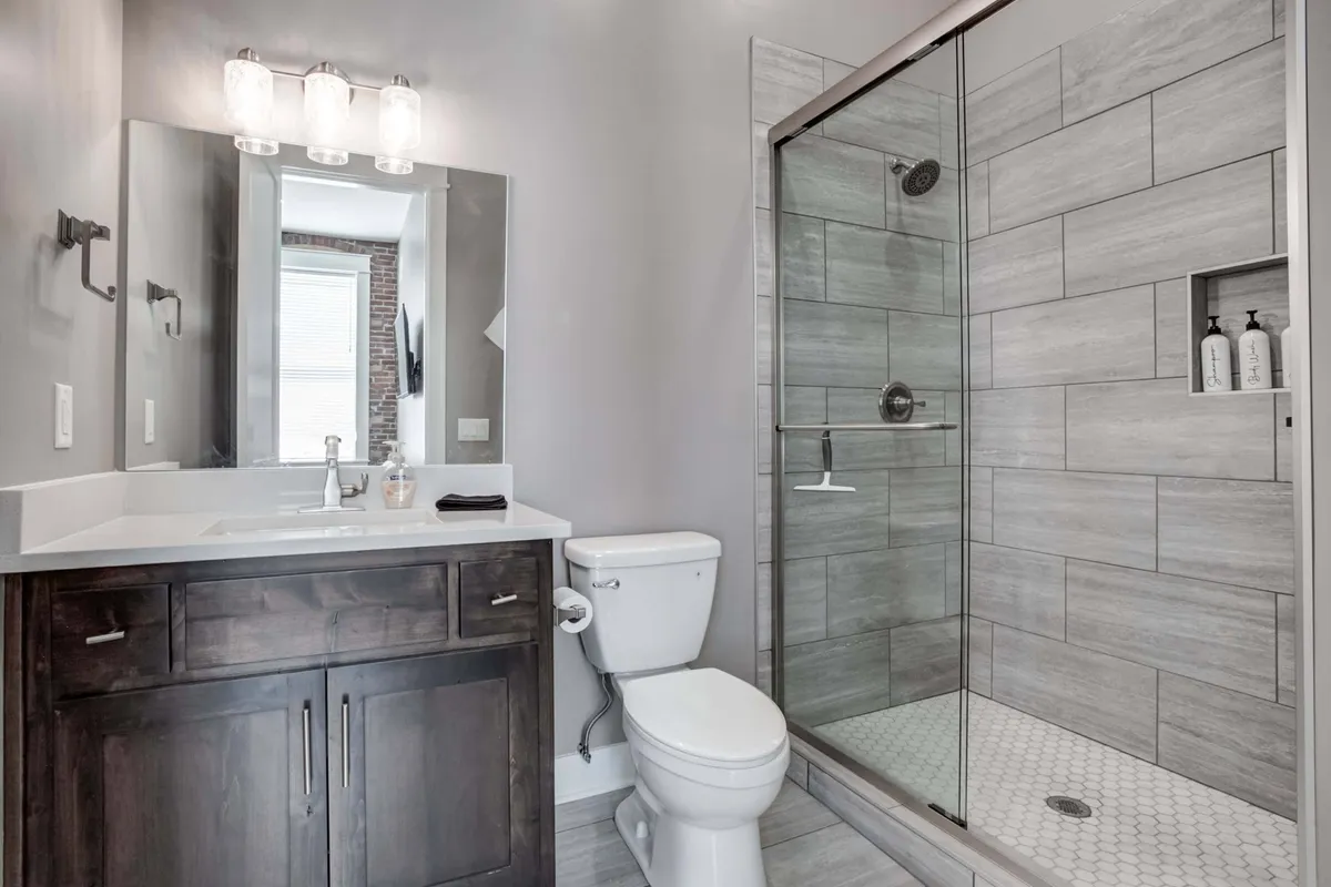 A modern bathroom with a glass shower enclosure, spacious vanity with sink, and a large mirror. The room is bathed in morning light, presenting a fresh and inviting space ideal for personal care routines.
